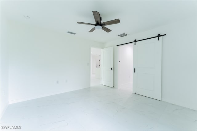 spare room with ceiling fan and a barn door