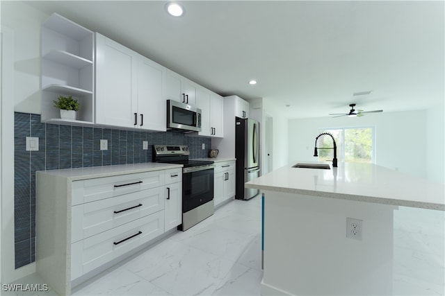 kitchen featuring ceiling fan, sink, a kitchen island with sink, appliances with stainless steel finishes, and white cabinets