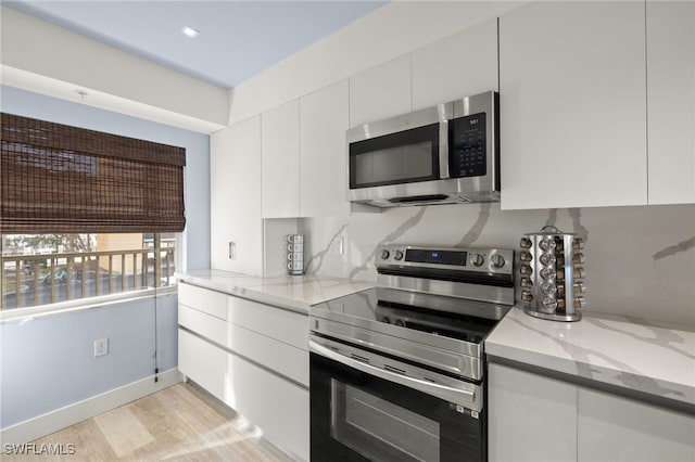 kitchen with appliances with stainless steel finishes, tasteful backsplash, white cabinetry, light stone counters, and light hardwood / wood-style floors