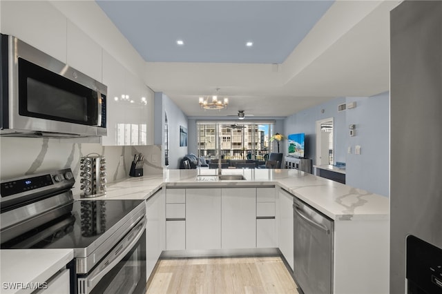 kitchen with hanging light fixtures, kitchen peninsula, stainless steel appliances, light hardwood / wood-style floors, and white cabinets