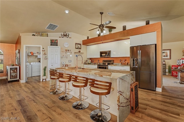 kitchen featuring white cabinets, appliances with stainless steel finishes, a kitchen bar, sink, and independent washer and dryer