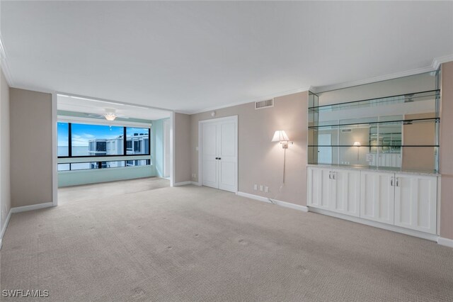 unfurnished living room with light carpet, ceiling fan, and ornamental molding