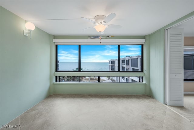 unfurnished room with ceiling fan and a water view