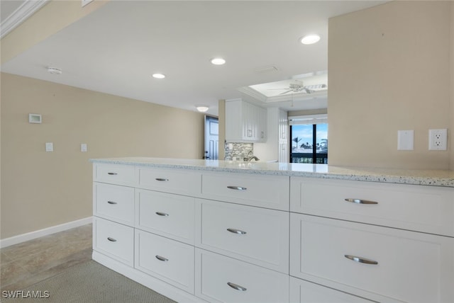 kitchen featuring kitchen peninsula, ceiling fan, light stone countertops, ornamental molding, and white cabinets