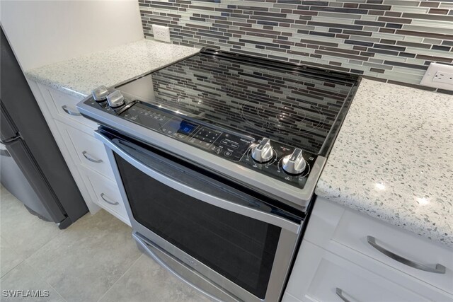 details with stainless steel range with electric cooktop, white cabinetry, decorative backsplash, and light stone countertops