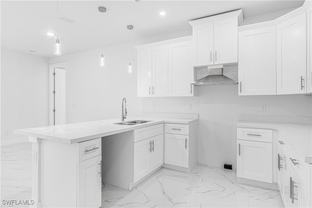 kitchen with pendant lighting, sink, wall chimney range hood, and white cabinets