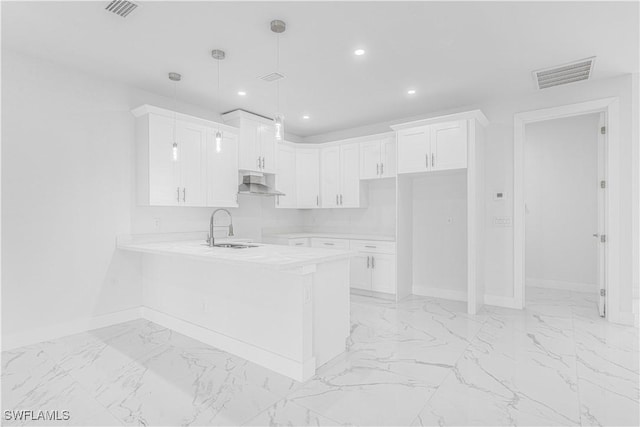 kitchen featuring kitchen peninsula, decorative light fixtures, wall chimney range hood, white cabinets, and sink