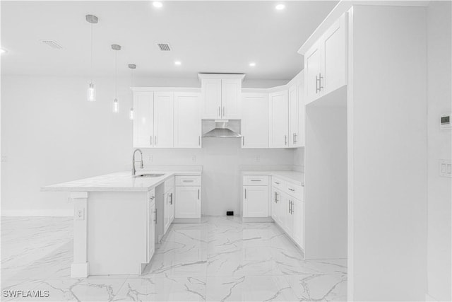 kitchen with sink, wall chimney range hood, white cabinets, and hanging light fixtures