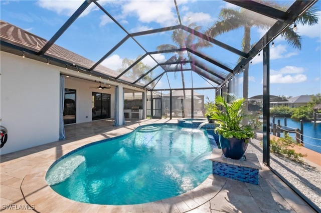 view of pool with ceiling fan, a patio, glass enclosure, a water view, and an in ground hot tub