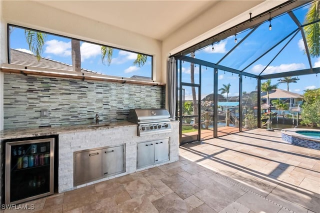 view of patio / terrace featuring a lanai, wine cooler, area for grilling, grilling area, and an in ground hot tub