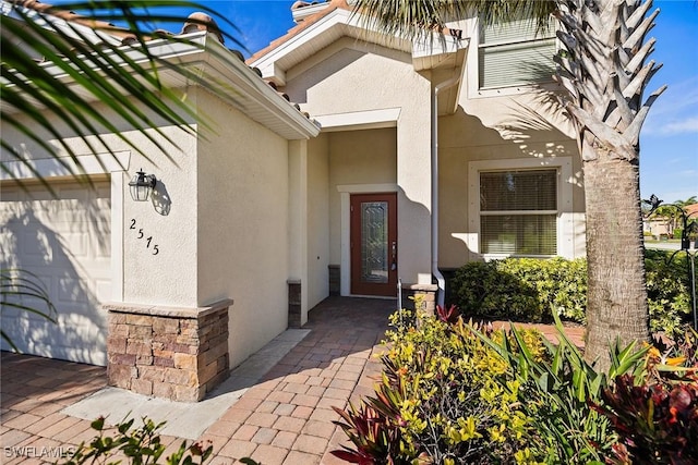 entrance to property with a garage, stone siding, and stucco siding