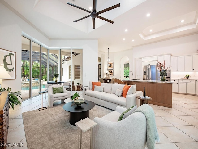 living room with sink, a high ceiling, light tile patterned floors, ceiling fan, and a tray ceiling