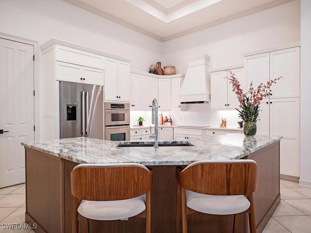 kitchen with premium range hood, white cabinetry, sink, stainless steel appliances, and a spacious island