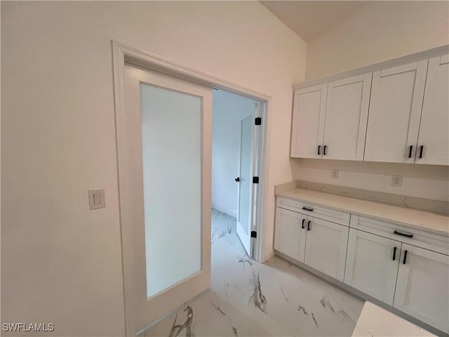 kitchen with vaulted ceiling, white cabinetry, and light stone counters