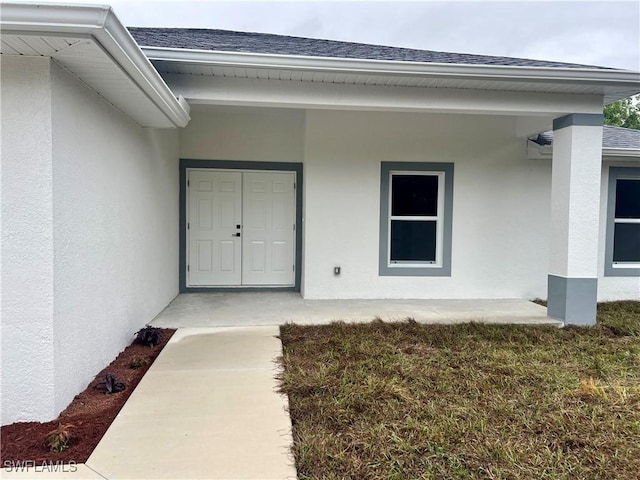 property entrance with stucco siding and roof with shingles