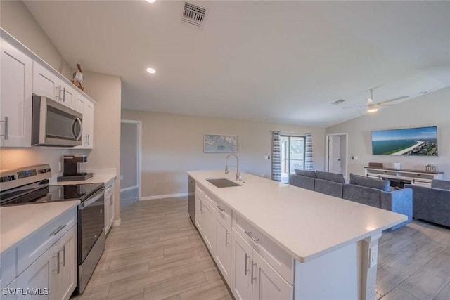 kitchen with lofted ceiling, sink, appliances with stainless steel finishes, an island with sink, and white cabinets