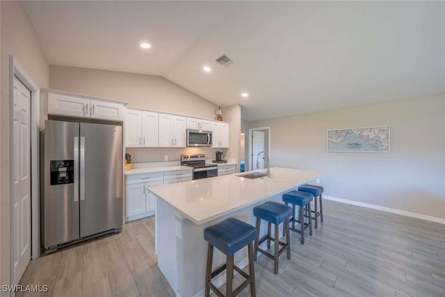 kitchen with sink, white cabinetry, a kitchen island with sink, appliances with stainless steel finishes, and a breakfast bar area