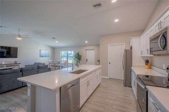 kitchen featuring stainless steel appliances, a kitchen island with sink, vaulted ceiling, white cabinets, and sink