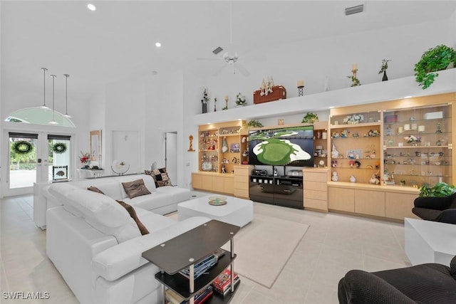 tiled living room with ceiling fan, french doors, and a towering ceiling