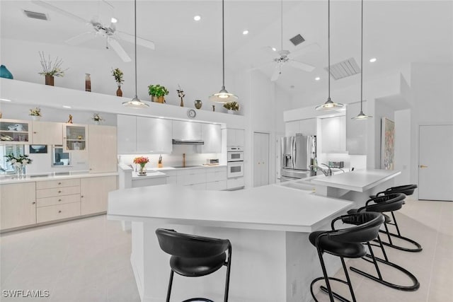 kitchen featuring hanging light fixtures, stainless steel fridge, a breakfast bar area, and a towering ceiling