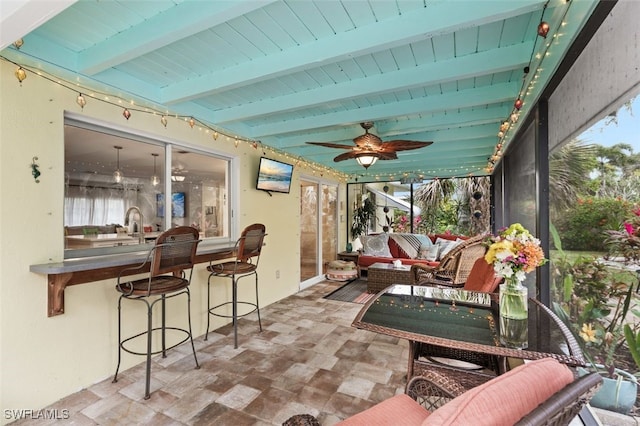 sunroom with ceiling fan and beam ceiling