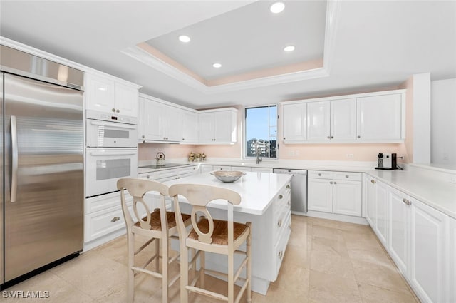 kitchen featuring a breakfast bar area, appliances with stainless steel finishes, a raised ceiling, a kitchen island, and white cabinets