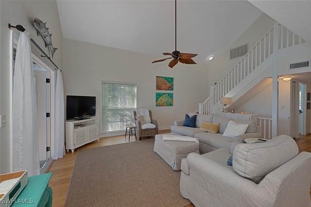 living room with ceiling fan, a towering ceiling, and light wood-type flooring