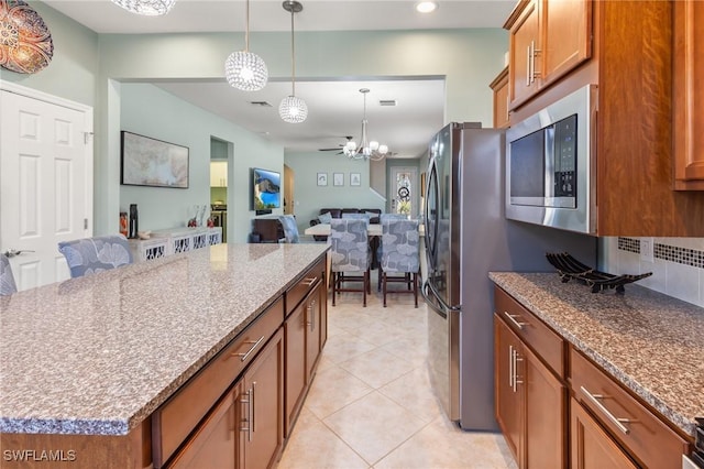 kitchen featuring pendant lighting, a center island, light tile patterned floors, stainless steel appliances, and light stone countertops