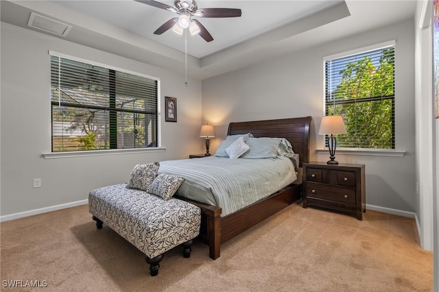 carpeted bedroom with ceiling fan and a raised ceiling