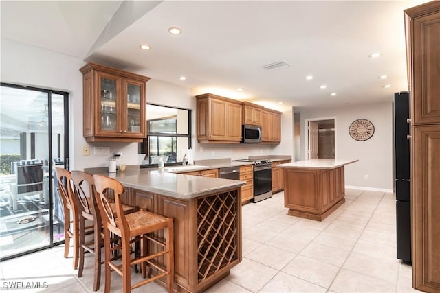 kitchen featuring stainless steel appliances, light tile patterned floors, a kitchen breakfast bar, and kitchen peninsula