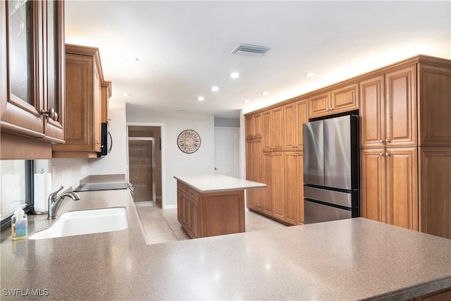 kitchen featuring sink, light tile patterned floors, stainless steel refrigerator, a center island, and kitchen peninsula