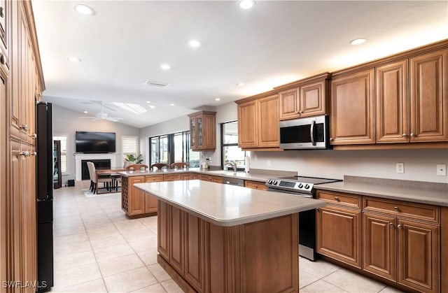 kitchen featuring lofted ceiling, light tile patterned floors, ceiling fan, stainless steel appliances, and a kitchen island