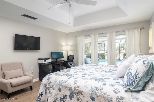 bedroom with ceiling fan, a tray ceiling, light hardwood / wood-style floors, and access to outside