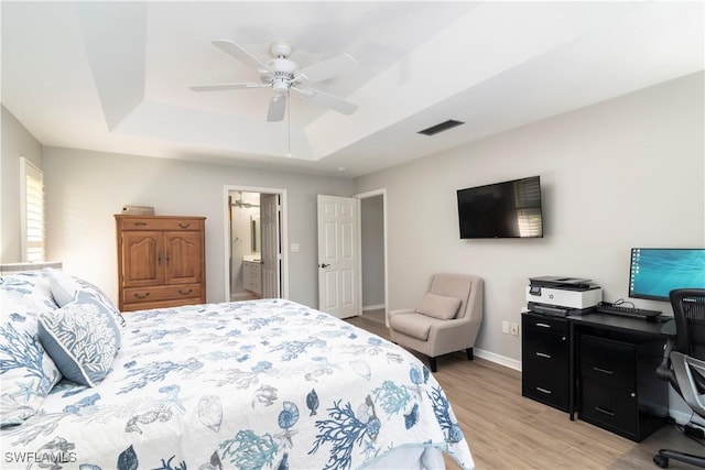 bedroom with ceiling fan, ensuite bathroom, a tray ceiling, and light hardwood / wood-style floors