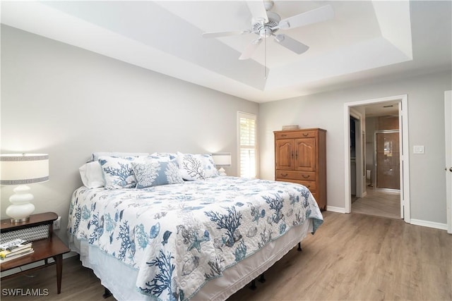 bedroom with hardwood / wood-style flooring, ceiling fan, and a tray ceiling