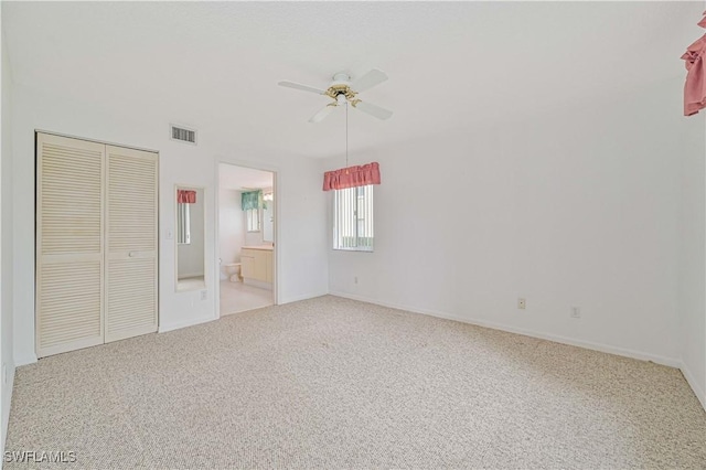 unfurnished bedroom featuring light carpet, visible vents, a ceiling fan, a closet, and ensuite bath