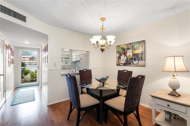 dining area with a textured ceiling, wood-type flooring, and a notable chandelier