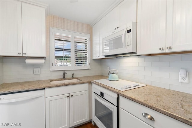 kitchen with white cabinetry, tasteful backsplash, white appliances, light stone counters, and sink