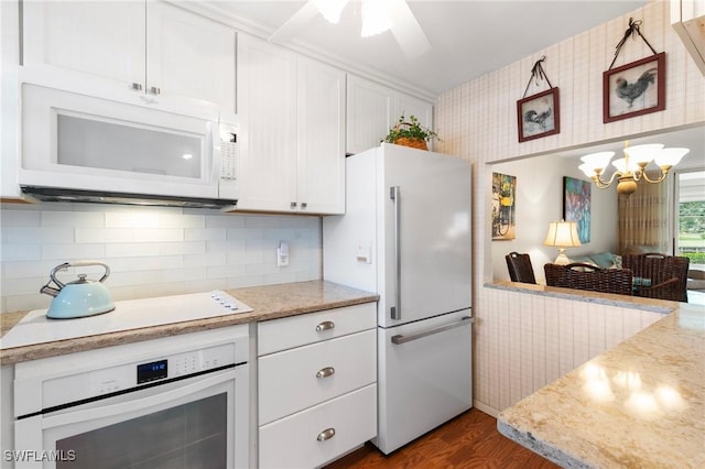 kitchen with tasteful backsplash, white appliances, light stone countertops, white cabinets, and dark hardwood / wood-style flooring