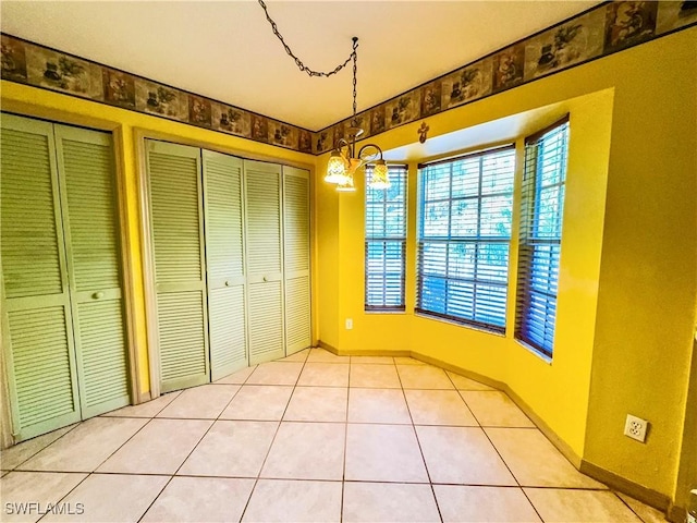 unfurnished bedroom with multiple closets, light tile patterned floors, and an inviting chandelier