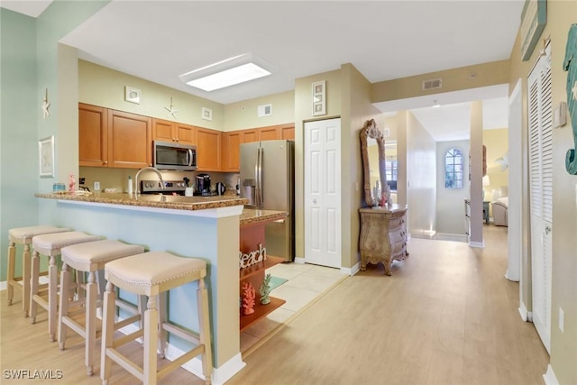 kitchen with kitchen peninsula, light hardwood / wood-style flooring, appliances with stainless steel finishes, a kitchen breakfast bar, and light stone counters