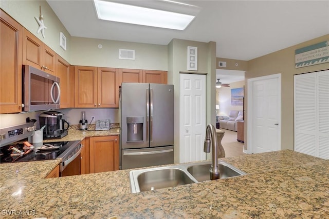 kitchen with light stone countertops, stainless steel appliances, kitchen peninsula, and sink