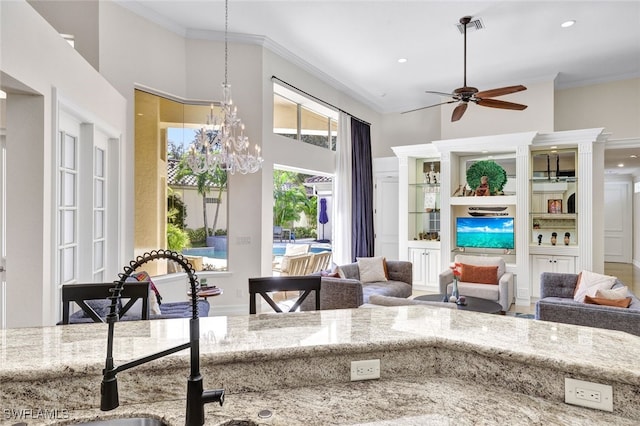 living room with a high ceiling, crown molding, sink, and ceiling fan with notable chandelier