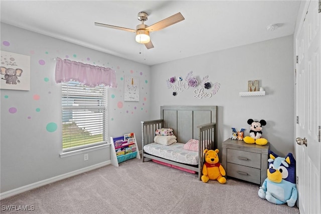 bedroom with a ceiling fan, light carpet, a crib, and baseboards