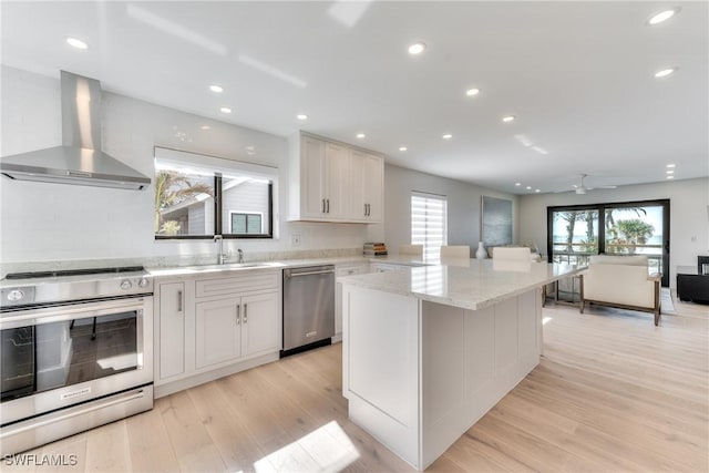 kitchen with ceiling fan, wall chimney range hood, white cabinetry, light hardwood / wood-style flooring, and stainless steel appliances