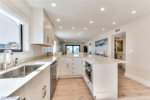 kitchen featuring kitchen peninsula, sink, white cabinetry, light hardwood / wood-style flooring, and stainless steel appliances