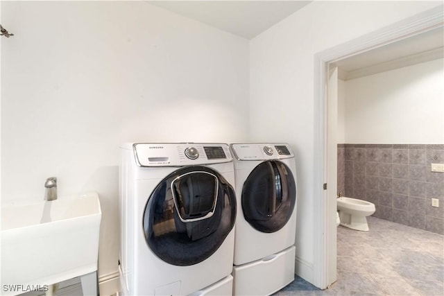 laundry area with tile walls, sink, and washing machine and clothes dryer