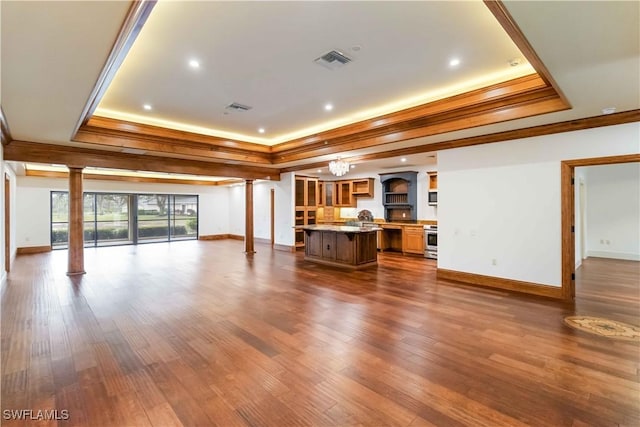 unfurnished living room featuring ornamental molding, wood-type flooring, a tray ceiling, and ornate columns