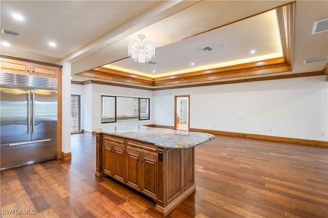 kitchen with light stone counters, a center island, a raised ceiling, and built in fridge