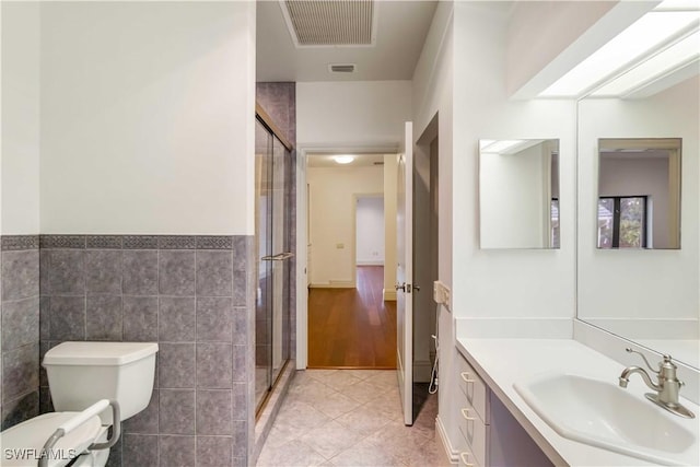 bathroom featuring tile patterned floors, toilet, a shower with shower door, tile walls, and vanity